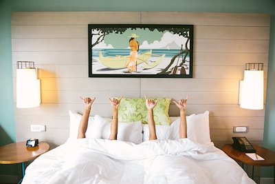 Two guest in hotel bed with hang loose sign